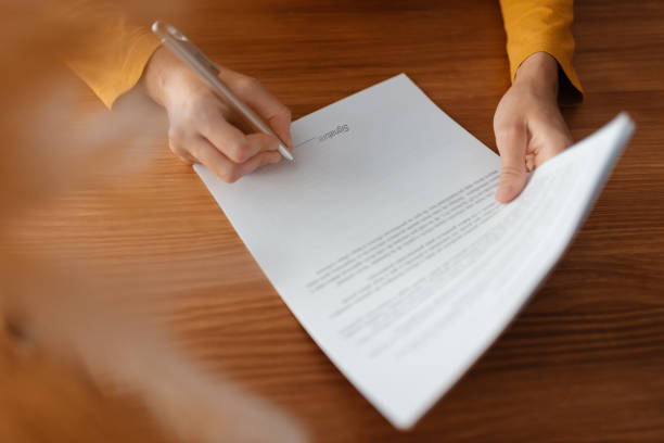 Close up image of an unrecognizable person signing a business document.